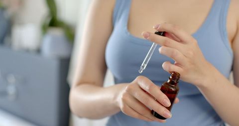 Woman Using Dropper for Skincare Routine in Bathroom