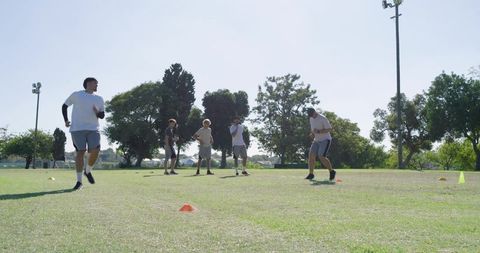 Male athletes performing cone agility drills on sunny park field for team conditioning