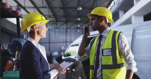 Supervisor and technician discussing safety in industrial workshop wearing hard hats