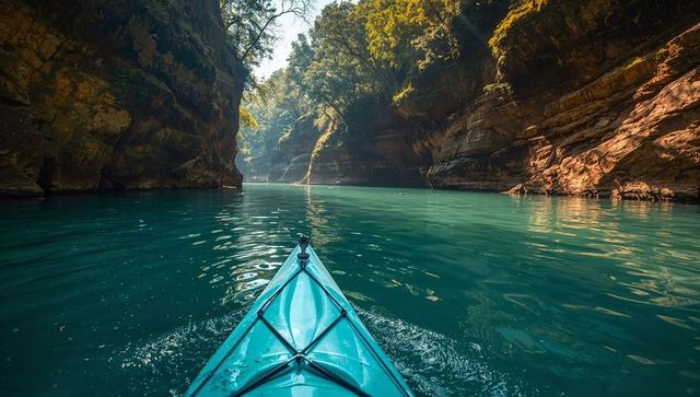 Gliding teal kayak bow through turquoise river canyon under sunlit cliffs for adventure travel