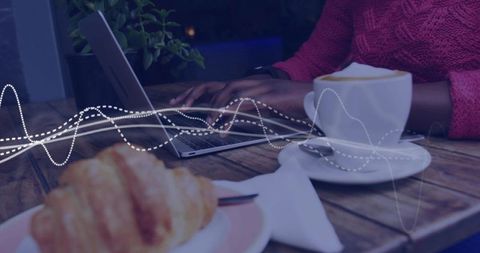 Cozy cafe remote work scene with woman typing on laptop beside cappuccino and croissant