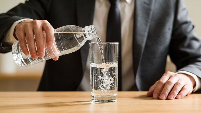 Executive pouring water into glass at desk in suit and tie for corporate wellness use