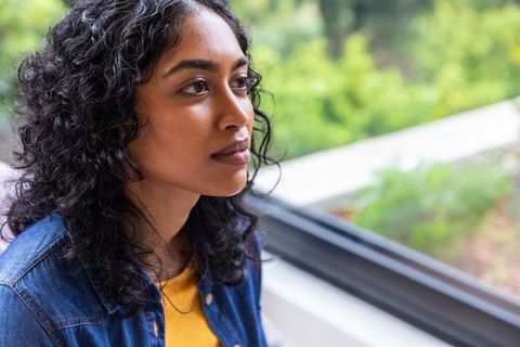 Thoughtful woman sitting by window in sunlit room