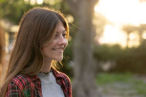 Sunlit young woman smiling in park at golden hour wearing plaid shirt and choker
