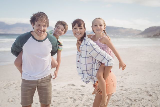 Young parents enjoying a sunny day at the beach with their children, piggybacking and smiling. Ideal for use in advertisements, travel brochures, family-oriented products, and websites promoting family vacations and outdoor activities.