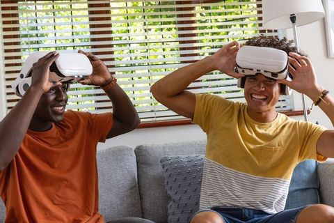 Multicultural male friends on couch wearing VR headsets, laughing and interacting
