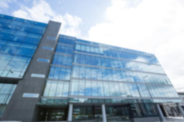 Blurred view of a modern office building with a glass facade reflecting the sky. Ideal for use in business presentations, corporate websites, and urban development projects to convey a sense of modernity and professionalism.