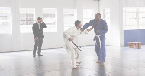 Instructor coaching student gripping collar in gi on dojo mats with observing coach