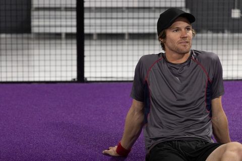 Male athlete resting on purple indoor court wearing cap and sportswear