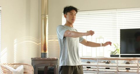 Asian man standing in sunlit rustic living room holding cord near wood stove cozy interior
