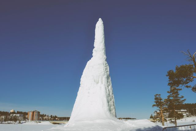 Tall ice structure stands majestically against a clear blue sky in a winter landscape. Ideal for travel blogs, nature magazines, and websites promoting winter destinations. Can also be used in educational materials about winter phenomena and natural ice formations.