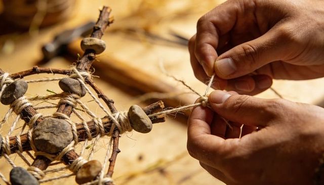 Hands tying twine on rustic twig web with river stones crafting boho wall hanging