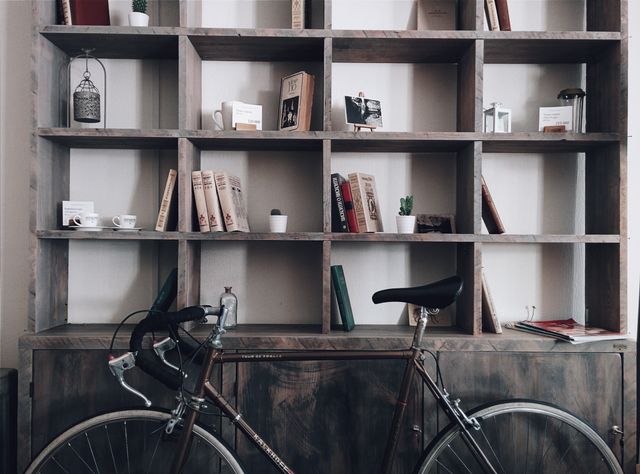 Vintage bike resting against large industrial bookshelf with assorted vintage decor items, books, and plants. Ideal for themes about urban living, interior design, organization, stylish home decor, minimalist lifestyle, and coffee shops.