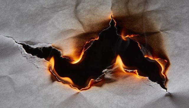 Macro of burning paper with charred edges, flickering flame and smoky torn hole