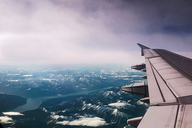 This image depicts the wing of an airplane, with a stunning aerial view of snowy mountains and lakes below. The scene captures the essence of travel, adventure, and the beauty of nature from above. Ideal for use in travel magazines, airline advertisements, blog posts about flying experiences, and nature documentaries.