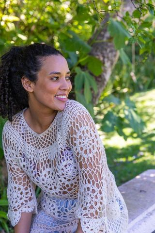 African american woman smiling on stone bench wearing crocheted top in leafy sunlit garden
