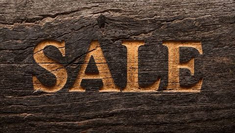 Rustic carved sale sign with amber glow on weathered wood plank, engraved serif letters