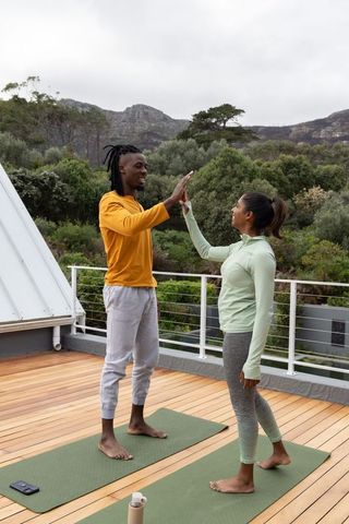 Multiracial couple high-fiving after rooftop yoga on wooden deck overlooking mountains
