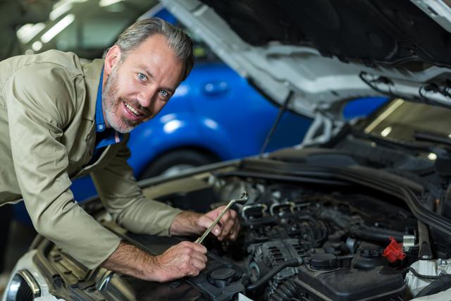 Mechanic smiling while servicing a automobile car engine in repair garage