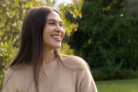 Young woman smiling and enjoying sunlit garden wearing beige knit sweater