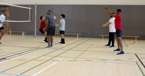 Diverse male team practicing volleyball in indoor gymnasium showing teamwork and training
