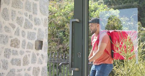 Courier carrying insulated red delivery backpack entering residential gate opening door