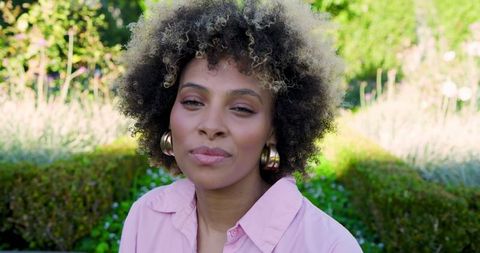Elegant Woman in Sunlit Garden with Gold Hoop Earrings
