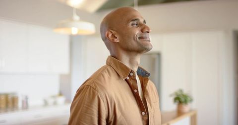 Serene mature man standing in bright modern kitchen wearing casual brown shirt
