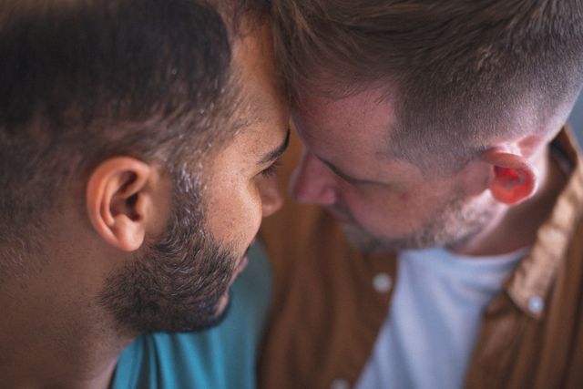 This image captures a tender moment between a diverse gay male couple embracing with their heads together, conveying love and intimacy. Ideal for use in articles, blogs, and campaigns promoting LGBTQ relationships, diversity, and the importance of affection and togetherness during quarantine or lockdown.