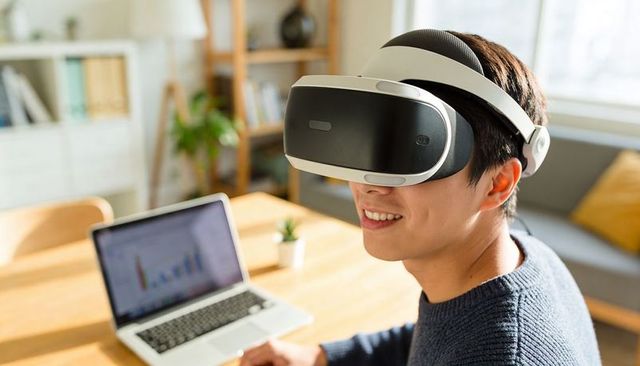 Smiling man wearing vr headset exploring virtual workspace with laptop business chart