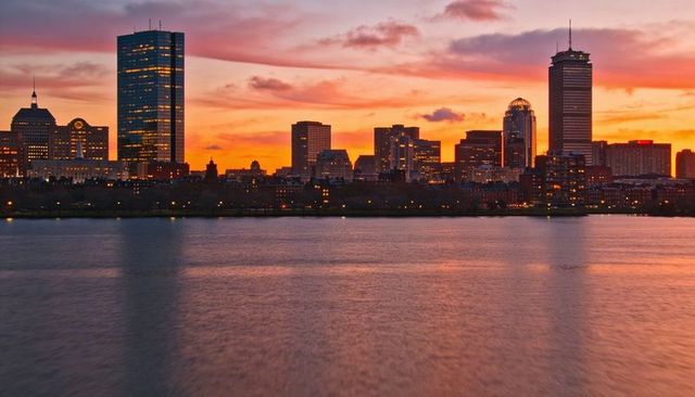 Sunset skyline reflecting across river with glowing skyscrapers, twilight city lights