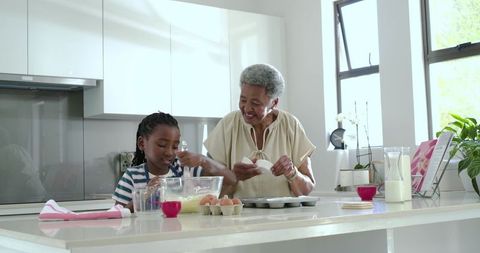 African american grandmother and granddaughter baking together in bright modern kitchen