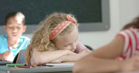 Girl resting on desk during class with studious classmates