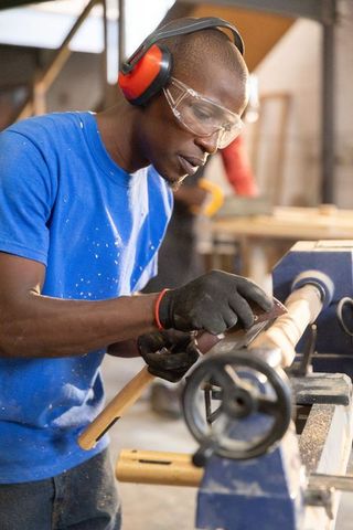 African american carpenter working on wood lathe sanding spindle wearing protective gear