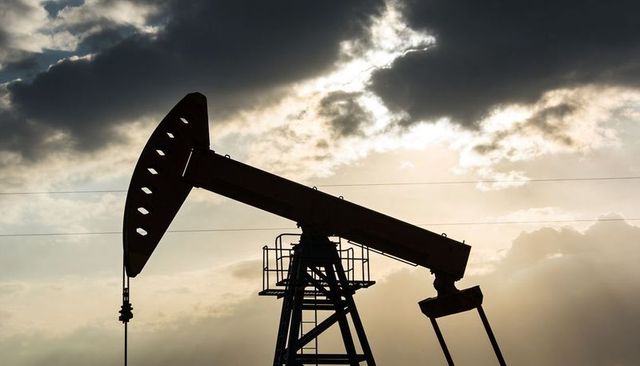 Backlit oil pumpjack silhouette at sunset with walking beam and horseshead against clouds