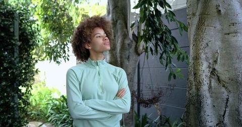 African american woman standing in garden with arms crossed gazing upward in mint pullover