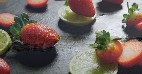 Juicy strawberries and limes on dark slate surface