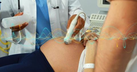 Pregnancy ultrasound scanning doctor using transducer on expectant patient abdomen with gel bottle