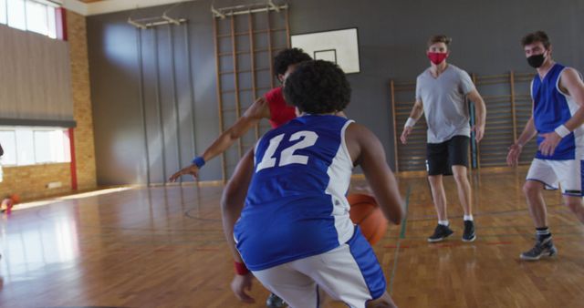 Youth basketball players competing in game on indoor court with coach watching. Players wearing sports uniforms and masks, indicating attention to safety and health protocols fitness, sports training, teamwork, and high school athletic programs illustrations. Useful for promoting youth sports activities, educational institutions, health and safety practices in sports.