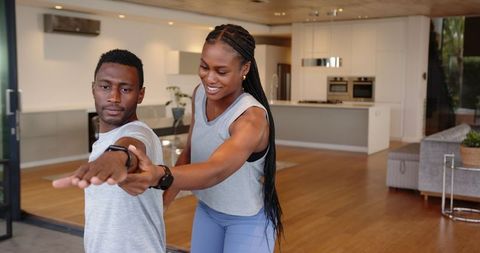 Personal Trainer Assisting Client with Stretching in Modern Living Room