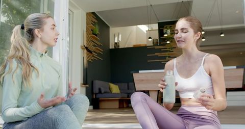 Two women chatting and cooling down after home workout while holding reusable water bottle