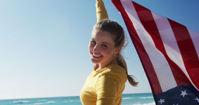 Woman enjoying beach holding American flag, ideal for celebrating national holidays, freedom, patriotic campaigns, travel promotions near oceans or lakes. Enhances content relating to summer activities, outdoor recreation, and national pride.