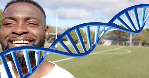 Smiling male athlete on sports field with blue DNA double helix overlay, genetics concept