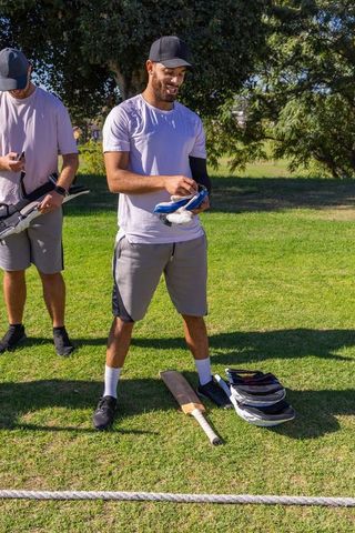 Two teammates adjusting batting gloves on sunny cricket field with bat and helmets