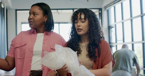 African women collaborating and unpacking bubble wrap in bright modern coworking studio