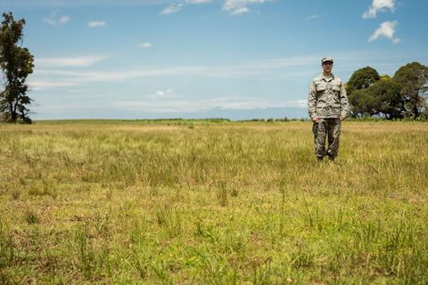 Solitary Soldier Standing in Open Grassland Wearing Camouflage Uniform Under Blue Sky