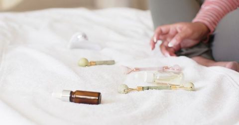 African american woman sitting on bed reaching jade rollers and serums for skincare ritual