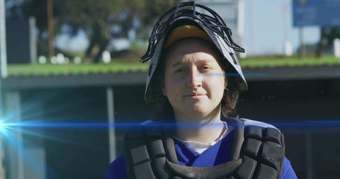 Woman catcher standing wearing helmet chest protector on baseball field with lens flare