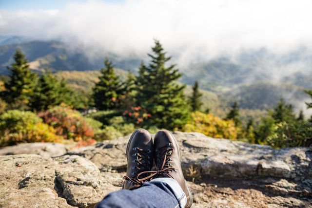 Hiker relaxing with boots in foreground overlooks mountainous landscape and cloudy sky. Perfect for use in travel blogs, outdoor adventure promotions, peaceful retreat advertisements, and scenic view calendars.