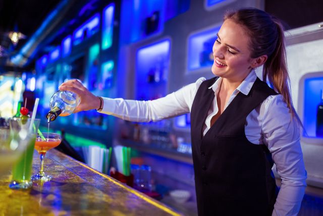 Beautiful bartender pouring drink in glass at nightclub